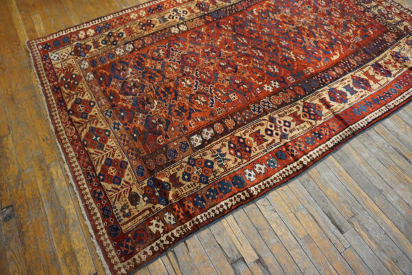 Red, blue, and tan geometric patterned low-pile rug on rustic wooden plank floors.