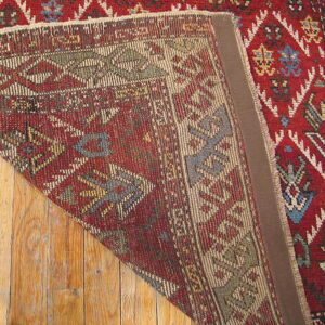 Geometric red and multicolor rug folded to show the tightly woven backside structure over wood flooring.