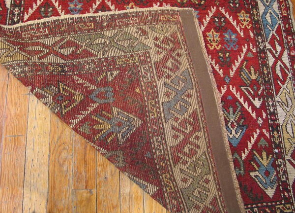 Geometric red and multicolor rug folded to show the tightly woven backside structure over wood flooring.