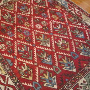 Low pile red rug with blue, cream, and yellow tribal geometric patterns lying on wood planks.