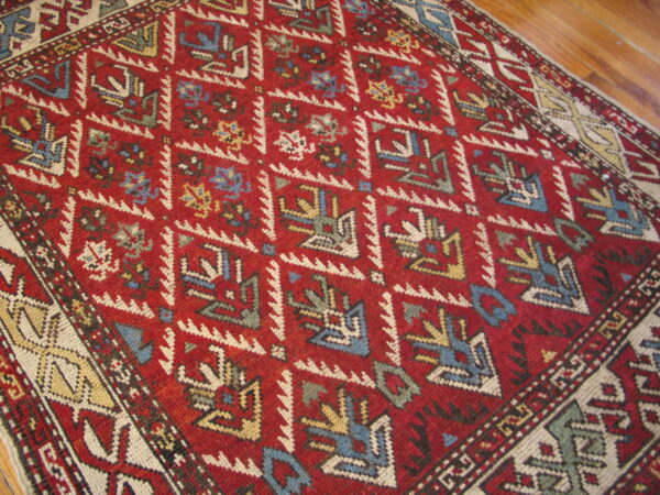 Low pile red rug with blue, cream, and yellow tribal geometric patterns lying on wood planks.