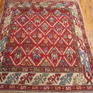 Geometric red area rug with tribal motifs in blue, cream, and gold laying on polished wood planks.