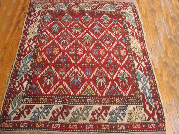 Geometric red area rug with tribal motifs in blue, cream, and gold laying on polished wood planks.