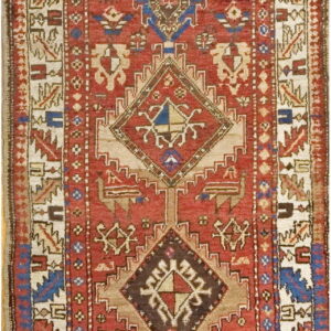 A long runner rug featuring stacked red and blue geometric diamond medallions on a rustic pile.