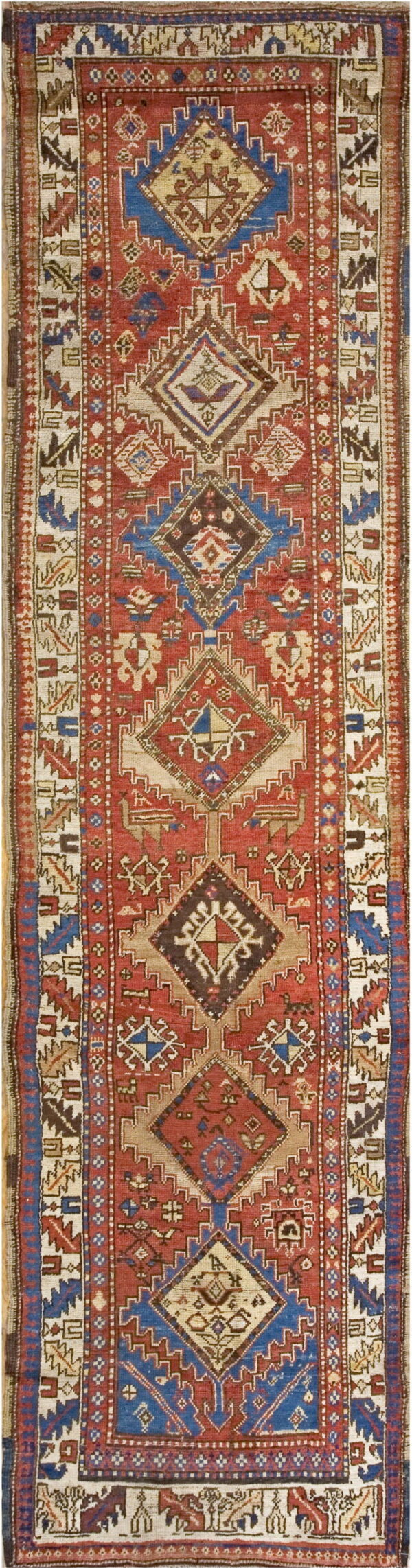 A long runner rug featuring stacked red and blue geometric diamond medallions on a rustic pile.