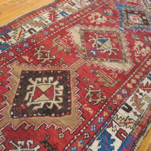 Red geometric runner featuring blue, brown, and cream patterns lies diagonally on a wood floor.