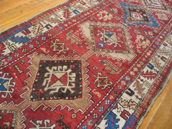 Red geometric runner featuring blue, brown, and cream patterns lies diagonally on a wood floor.