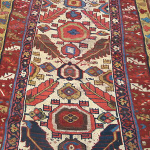 Red, cream, and navy geometric runner rug featuring central serrated motifs on wood plank flooring.