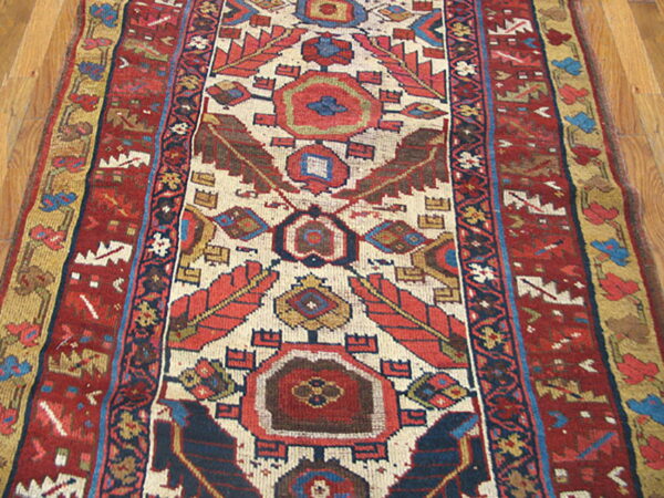 Red, cream, and navy geometric runner rug featuring central serrated motifs on wood plank flooring.