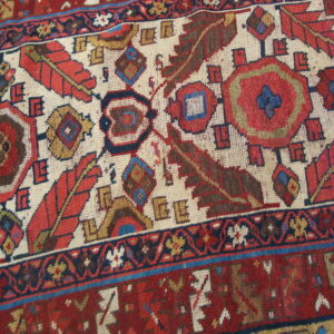 Geometric rug pattern featuring stylized feathers and medallions in red, navy, brown, and cream.