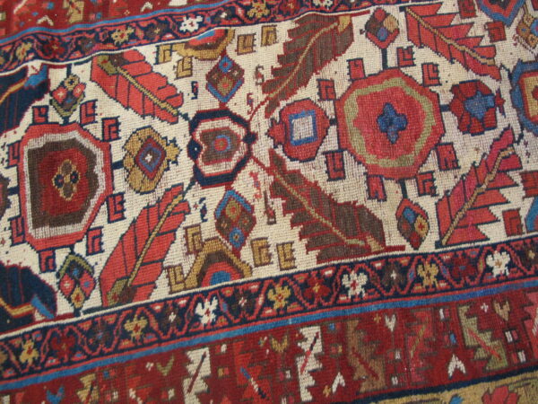 Geometric rug pattern featuring stylized feathers and medallions in red, navy, brown, and cream.