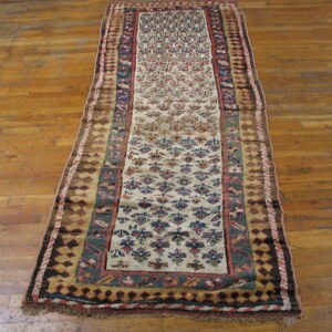 Narrow runner rug with a cream patterned field and multicolored borders rests on polished hardwood planks.