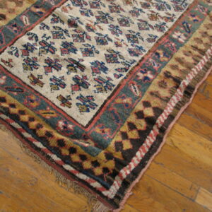 Low-pile rug in cream, deep teal, and red geometric patterns rests on distressed wood flooring.