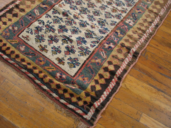 Low-pile rug in cream, deep teal, and red geometric patterns rests on distressed wood flooring.
