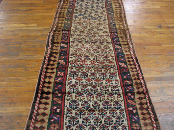Long traditional runner with red, blue, and ivory repeating patterns resting on light brown hardwood floors.