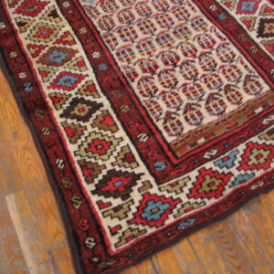 High-contrast geometric rug in red, cream, and blue placed on distressed wooden floorboards.