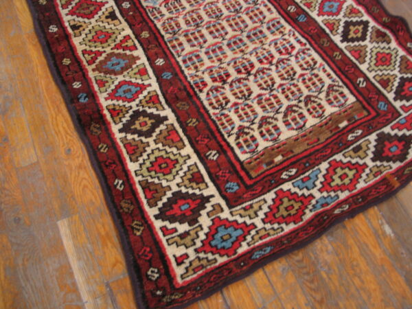 High-contrast geometric rug in red, cream, and blue placed on distressed wooden floorboards.