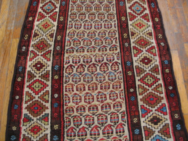 Multicolor runner rug featuring geometric borders and a central field of repeating stylized house motifs on wood flooring.
