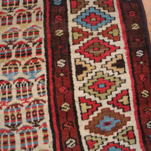 Close-up of a patterned rug in red, cream, blue, and brown geometric stripes over hardwood flooring.