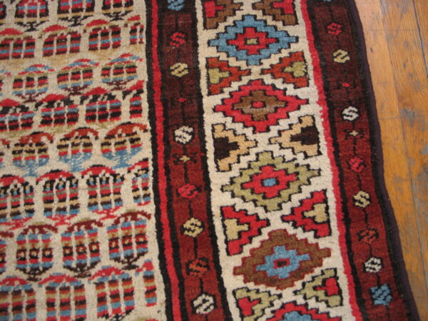 Close-up of a patterned rug in red, cream, blue, and brown geometric stripes over hardwood flooring.