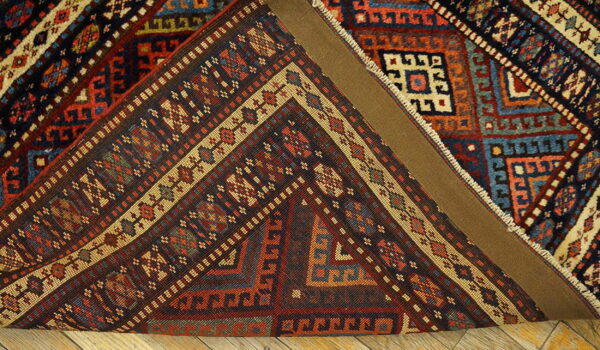 A multi-colored traditional geometric rug corner is folded, revealing a brown canvas backing over wood flooring.