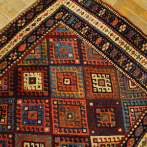 Geometric patterned rug in shades of blue, red, and tan displayed on rustic light wood flooring.