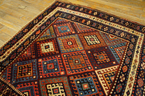 Geometric rug with nested square designs in blue, red, orange, and cream on rustic wood plank flooring.