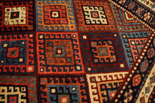 High-pile rug detail showing repeating geometric medallions in navy, rust, teal, and cream colors.