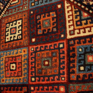 Geometric rug detail showing repeating hooked squares in navy, teal, brick red, and ivory colors.