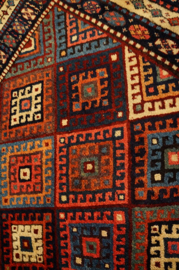 Geometric rug detail showing repeating hooked squares in navy, teal, brick red, and ivory colors.