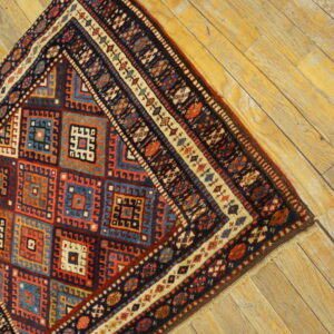 Section of a low-pile geometric rug with red and navy colors visible on golden wood planks.