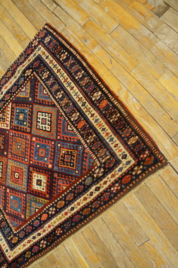 Section of a low-pile geometric rug with red and navy colors visible on golden wood planks.