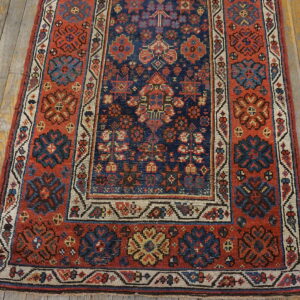 Traditional rug with a navy blue field and a rust red border featuring geometric and floral patterns on wood flooring.