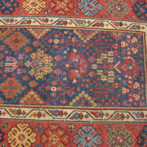Close-up of a rug featuring traditional geometric patterns in deep blue, rust red, cream, and yellow.