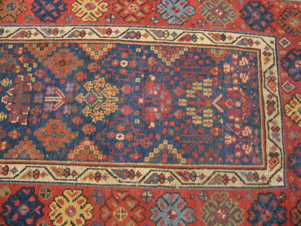 Close-up of a rug featuring traditional geometric patterns in deep blue, rust red, cream, and yellow.