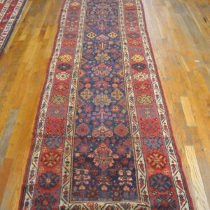 Long, low-pile runner rug with complex red and navy geometric tribal patterns on a wood plank floor.