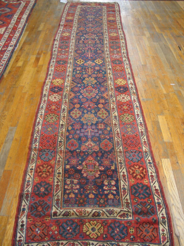 Long, low-pile runner rug with complex red and navy geometric tribal patterns on a wood plank floor.