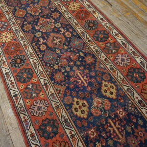 Navy blue runner rug with intricate red, cream, and yellow geometric motifs on rustic wooden floors.