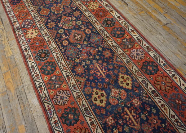 Navy blue runner rug with intricate red, cream, and yellow geometric motifs on rustic wooden floors.