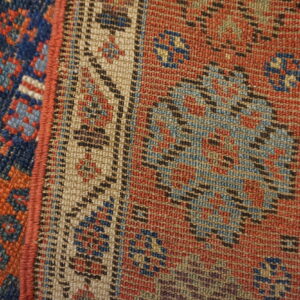 Tightly woven rug detail showing contrasting blue, rust red, and beige geometric borders separated by a red edge.