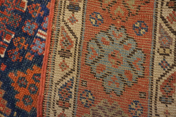 Tightly woven rug detail showing contrasting blue, rust red, and beige geometric borders separated by a red edge.
