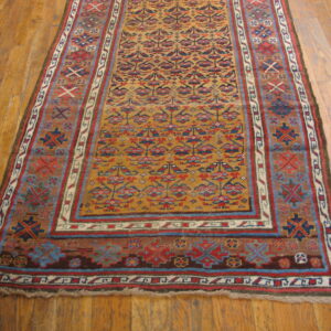 Mustard runner rug with complex red, blue, and brown geometric patterns lying on wooden floorboards.