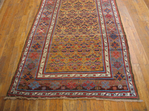 Mustard runner rug with complex red, blue, and brown geometric patterns lying on wooden floorboards.