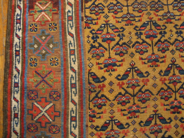 Detailed close-up of a low-pile rug in mustard yellow, red, dark blue, and tan geometric patterns next to wood.