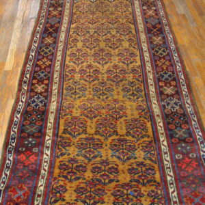 Low-pile runner with gold floral patterns and geometric maroon borders on light wood floorboards.