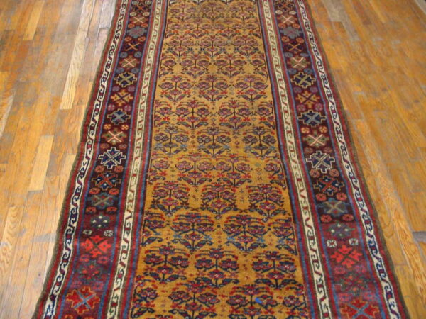 Low-pile runner with gold floral patterns and geometric maroon borders on light wood floorboards.
