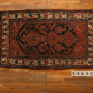 Rectangular dark navy and rust geometric rug with complex central medallions laid flat on warm wood planks.