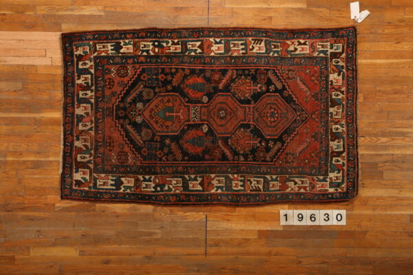 Rectangular dark navy and rust geometric rug with complex central medallions laid flat on warm wood planks.