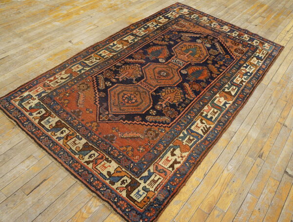 A detailed navy and terracotta geometric rug with animal figures lies on a distressed light wood floor.
