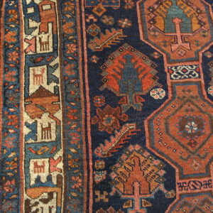 Navy blue rug with rust geometric medallions and detailed borders rests on light hardwood flooring.